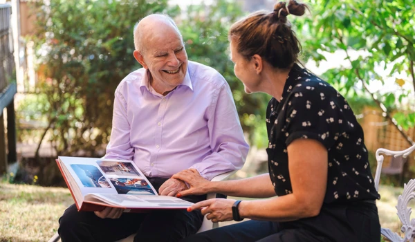 Smiling Older Man And Woman Sitting In Garden Looking Through Photo Album