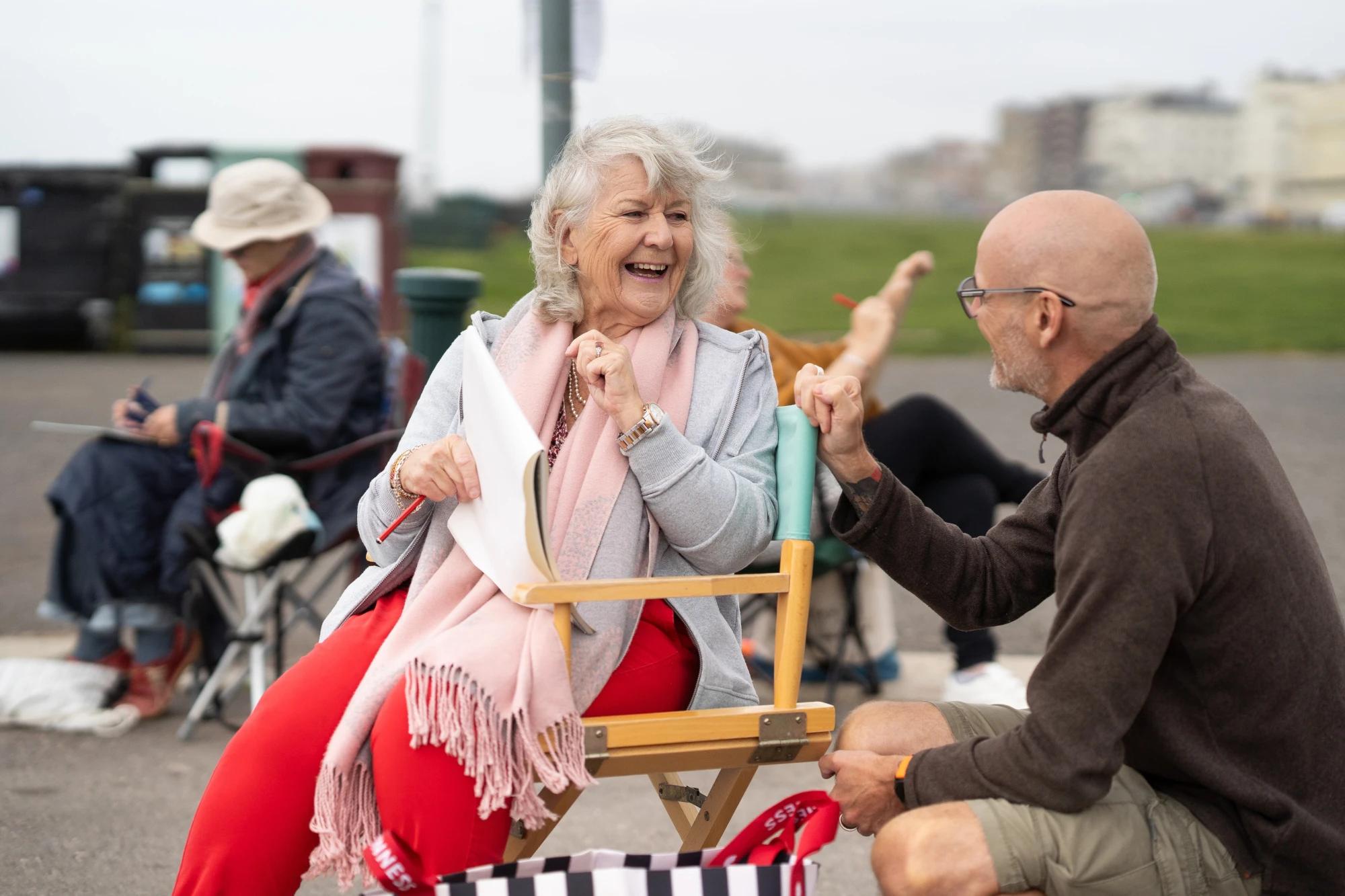 Older woman smiling whilst sitting in chair outdoors talking to man